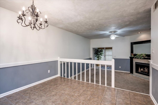 carpeted empty room featuring visible vents, a tiled fireplace, ceiling fan with notable chandelier, a textured ceiling, and baseboards