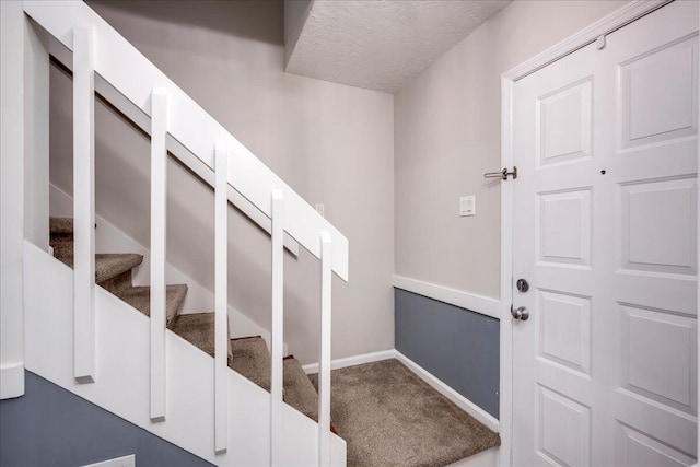 carpeted entryway featuring baseboards, a textured ceiling, and stairs