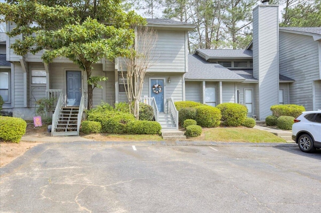 townhome / multi-family property featuring uncovered parking, roof with shingles, and a chimney