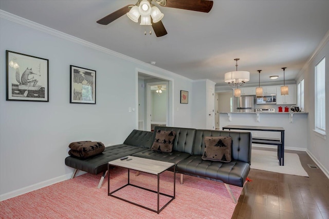 living room featuring dark hardwood / wood-style flooring, a healthy amount of sunlight, ceiling fan with notable chandelier, and ornamental molding