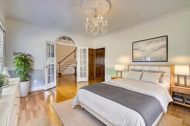 bedroom with light hardwood / wood-style floors, french doors, crown molding, and a chandelier