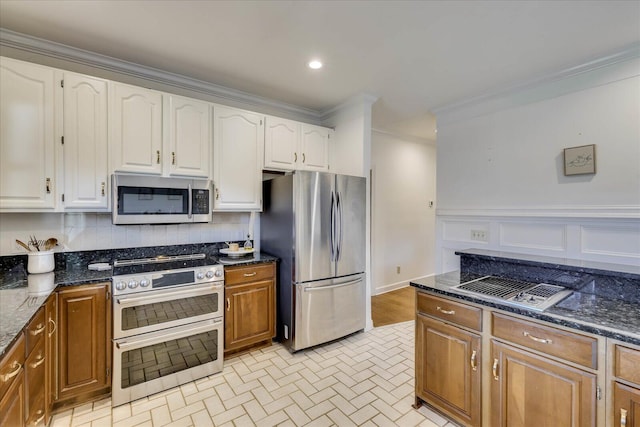 kitchen with appliances with stainless steel finishes, white cabinets, decorative backsplash, ornamental molding, and dark stone countertops