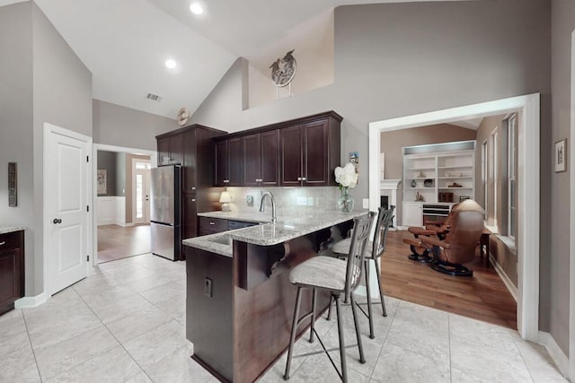 3039 Tarleton Ct, Beech Island, SC 29842 - kitchen with freestanding refrigerator, high vaulted ceiling, light stone countertops, a kitchen breakfast bar, and dark brown cabinetry