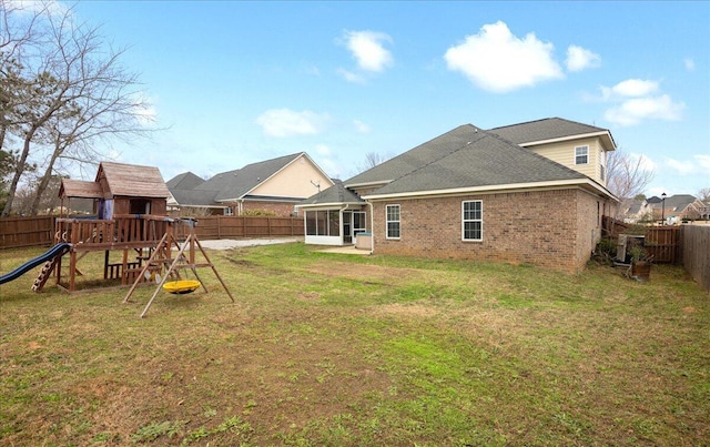 back of property with a sunroom, a playground, and a lawn