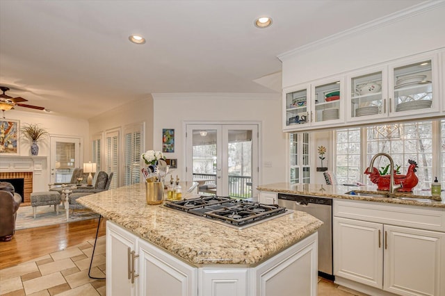 kitchen featuring a kitchen island, appliances with stainless steel finishes, light stone countertops, a brick fireplace, and a sink