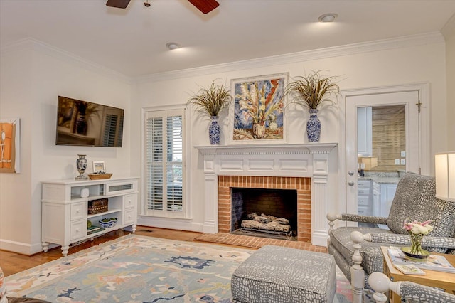 living area with crown molding, light wood-style flooring, a brick fireplace, ceiling fan, and baseboards