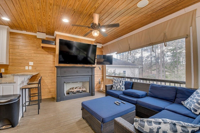 living room with wooden ceiling, wood walls, exterior fireplace, and light wood finished floors