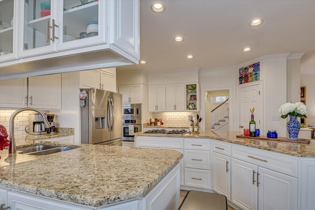 kitchen with white cabinets, ornamental molding, a peninsula, stainless steel appliances, and a sink