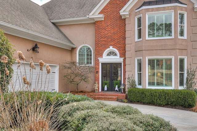 doorway to property featuring french doors, a shingled roof, brick siding, and stucco siding