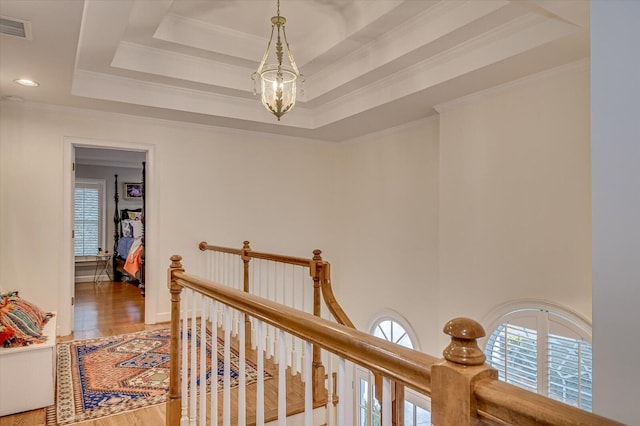 hallway with wood finished floors, visible vents, an upstairs landing, a raised ceiling, and crown molding