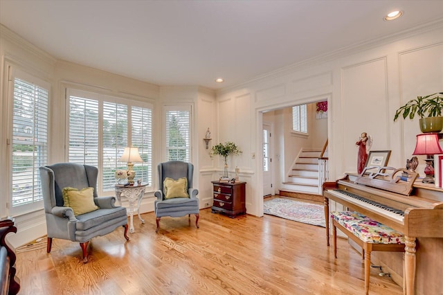 sitting room with crown molding, recessed lighting, a decorative wall, light wood-type flooring, and stairs