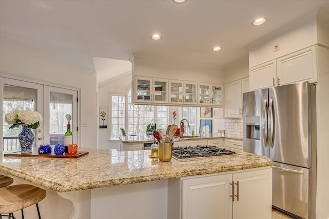 kitchen featuring white cabinets, light stone counters, glass insert cabinets, stainless steel appliances, and a sink