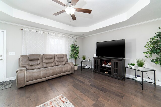 living room featuring a tray ceiling, crown molding, ceiling fan, and dark wood-type flooring