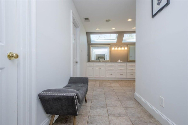 bathroom featuring a skylight, visible vents, baseboards, tile patterned floors, and double vanity