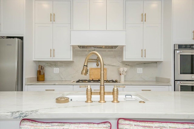 kitchen featuring appliances with stainless steel finishes, decorative backsplash, white cabinetry, and light stone countertops