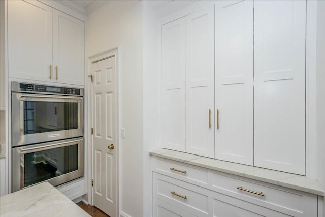 kitchen featuring stainless steel double oven, light stone countertops, and white cabinets