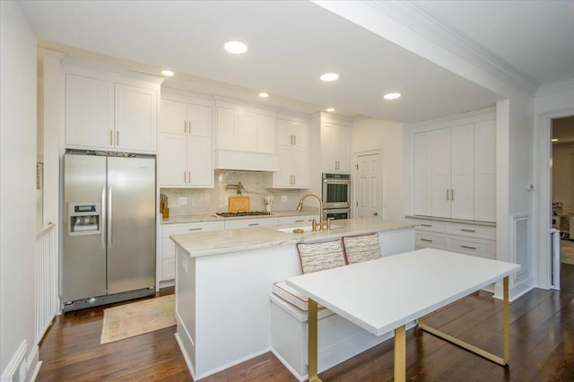 kitchen with an island with sink, dark wood-type flooring, stainless steel appliances, white cabinetry, and a sink