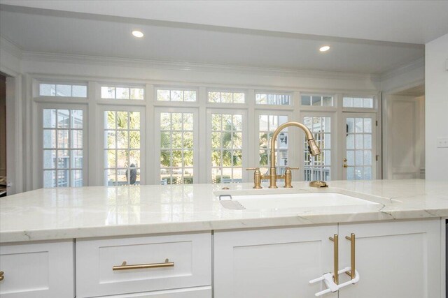 kitchen with light stone counters, recessed lighting, ornamental molding, white cabinetry, and a sink