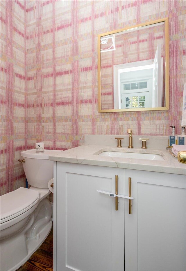 half bath with vanity, toilet, and wallpapered walls