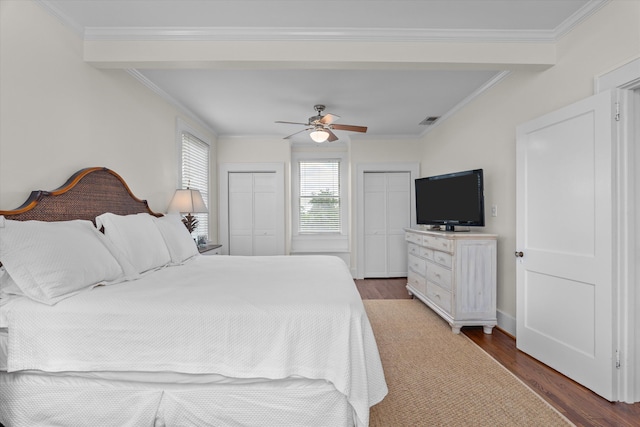 bedroom featuring crown molding, two closets, wood finished floors, and visible vents