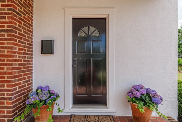 doorway to property featuring stucco siding and brick siding