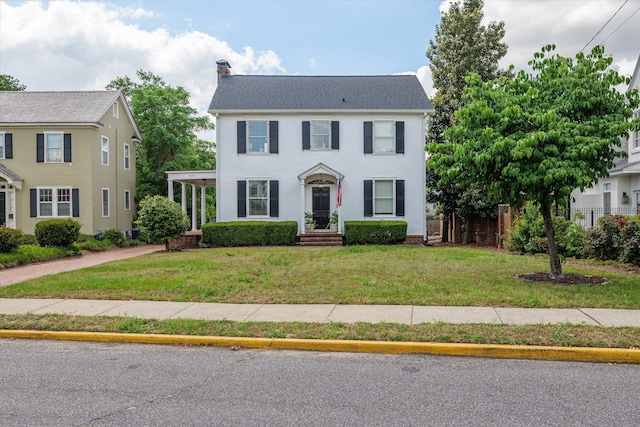 colonial inspired home with fence, a chimney, and a front lawn
