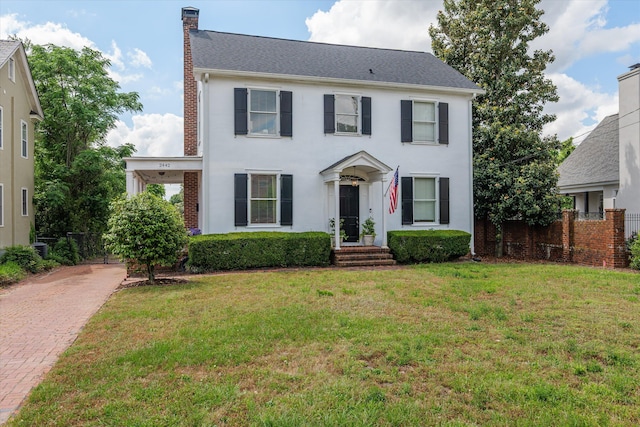 colonial-style house with fence, a chimney, stucco siding, and a front lawn