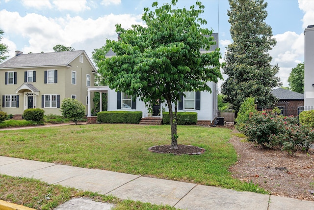 colonial home featuring stucco siding, fence, and a front lawn