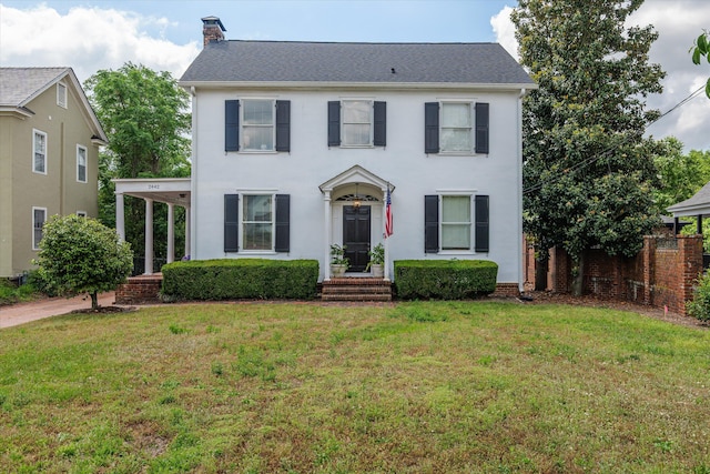 colonial inspired home with stucco siding, a front lawn, fence, and a chimney