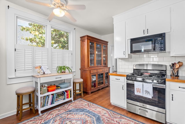 kitchen with black microwave, stainless steel range with gas cooktop, a ceiling fan, light wood-type flooring, and backsplash