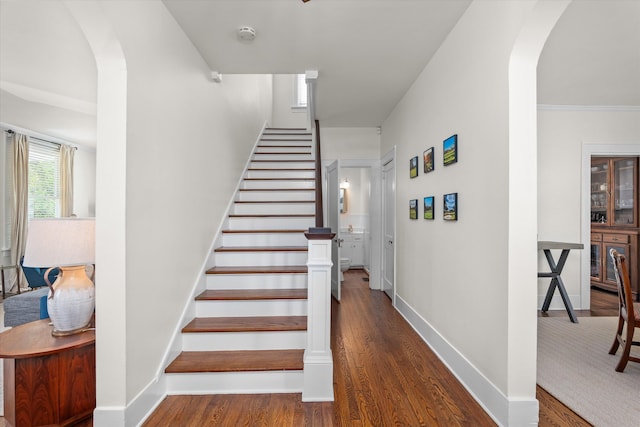stairs featuring baseboards, arched walkways, and wood finished floors