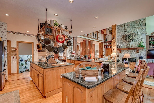 kitchen featuring kitchen peninsula, dark stone countertops, a fireplace, light hardwood / wood-style floors, and a kitchen island