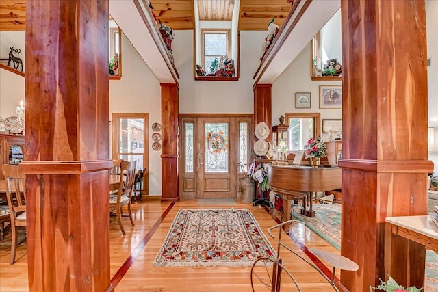 foyer with ornate columns, wooden ceiling, a high ceiling, and light wood-type flooring