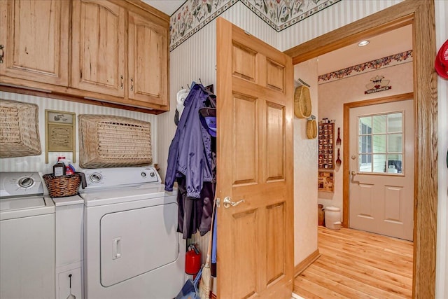 clothes washing area with cabinets, light wood-type flooring, and washing machine and clothes dryer