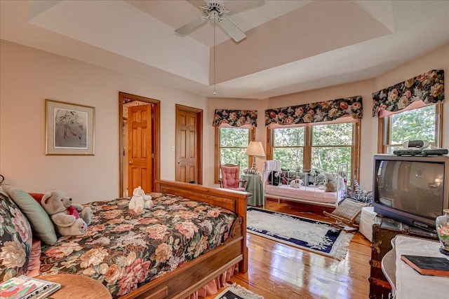 bedroom with hardwood / wood-style floors, a raised ceiling, and ceiling fan