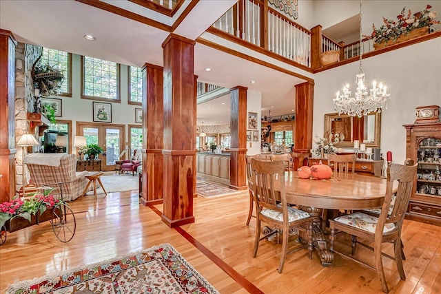 dining room with a chandelier, a high ceiling, light wood-type flooring, and ornate columns