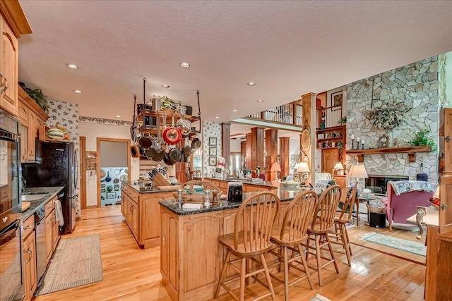 kitchen with kitchen peninsula, dark stone counters, a fireplace, light hardwood / wood-style floors, and a breakfast bar area