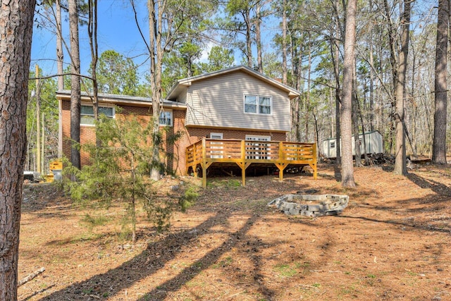 rear view of property with brick siding, a fire pit, and a deck