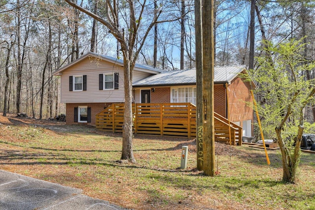 tri-level home with a wooden deck, brick siding, metal roof, and a front yard