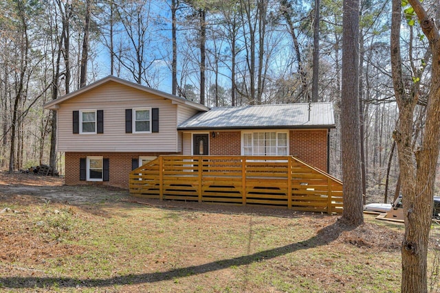 tri-level home featuring brick siding, a wooden deck, and metal roof