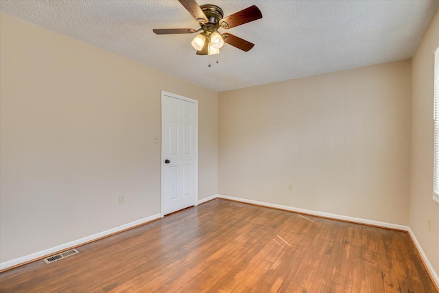 empty room with ceiling fan, visible vents, baseboards, and wood finished floors