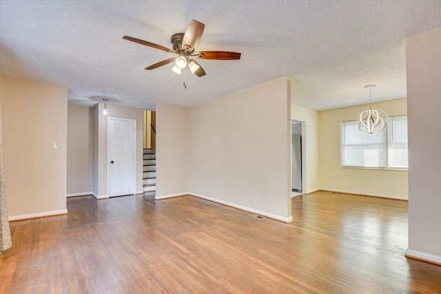 unfurnished room with baseboards, wood-type flooring, stairs, and ceiling fan with notable chandelier