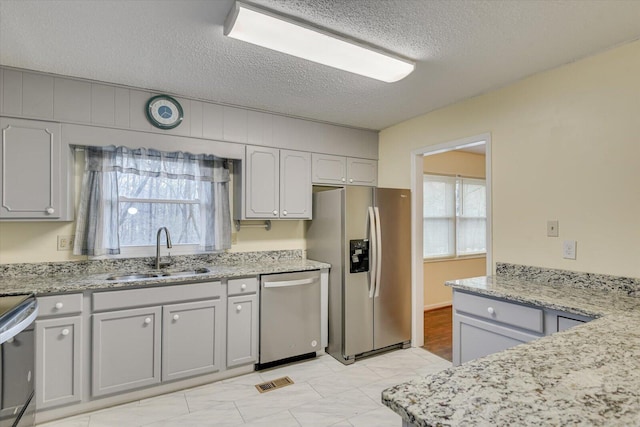 kitchen with visible vents, light stone countertops, appliances with stainless steel finishes, a textured ceiling, and a sink