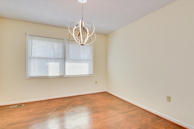 unfurnished room with a wealth of natural light, visible vents, an inviting chandelier, and wood finished floors