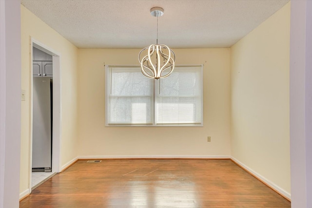 unfurnished dining area featuring visible vents, baseboards, wood finished floors, a notable chandelier, and a textured ceiling