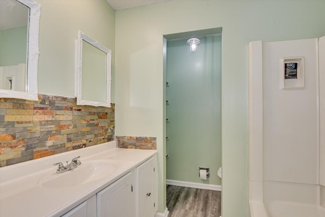 bathroom with vanity, wood finished floors, a textured ceiling, toilet, and tasteful backsplash