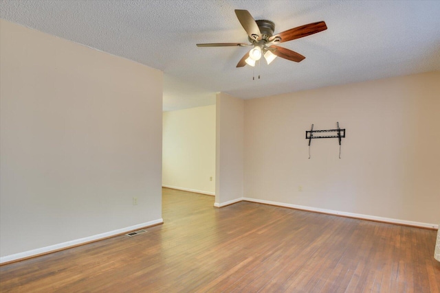 empty room featuring visible vents, a textured ceiling, wood finished floors, baseboards, and ceiling fan