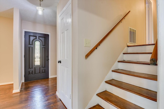 foyer entrance with visible vents, a textured ceiling, hardwood / wood-style floors, stairway, and baseboards