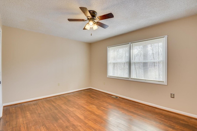 empty room with a textured ceiling, baseboards, wood-type flooring, and ceiling fan