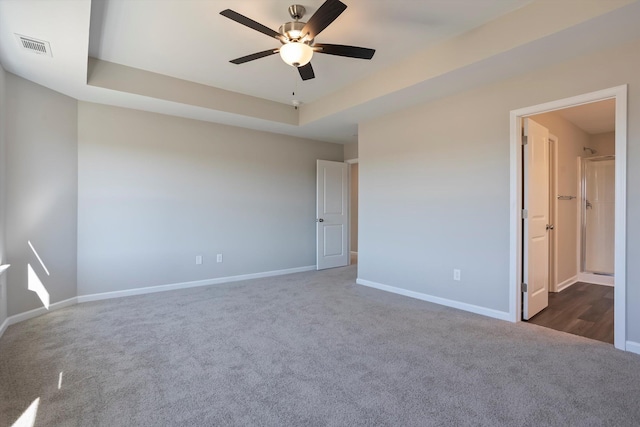 unfurnished bedroom with dark colored carpet, a raised ceiling, ensuite bath, and baseboards